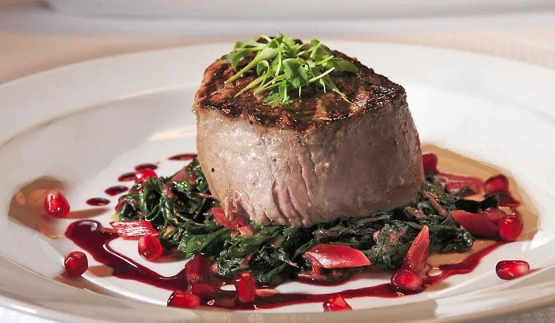 Bank restaurant plated filet with sautéed greens and pomegranate reduction