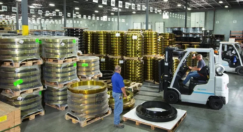 Stacked brass and black steel pipe flanges in industrial warehouse with forklift