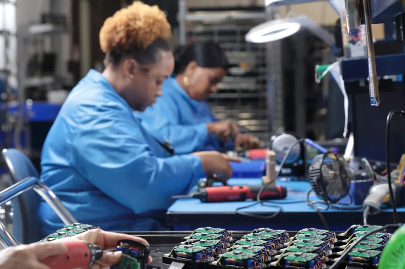Electronic assembly technicians soldering green circuit boards at illuminated workbench
