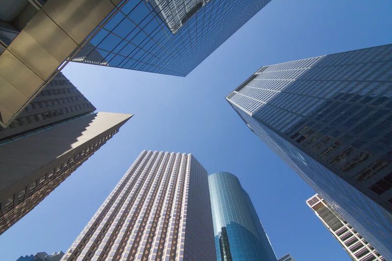 worm's-eye view of glass curtain-wall skyscrapers and cylindrical tower against clear blue sky