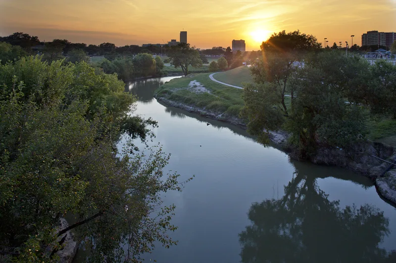 Calm river winding through lush parkland beneath vivid golden dusk sky