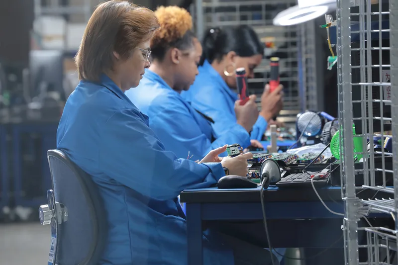 Electronic assembly technicians in blue uniforms inspecting circuit boards at workbench
