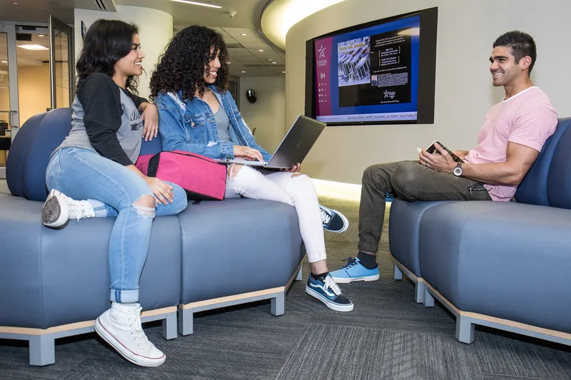 Students socializing in modern college lounge sharing laptop on upholstered seating