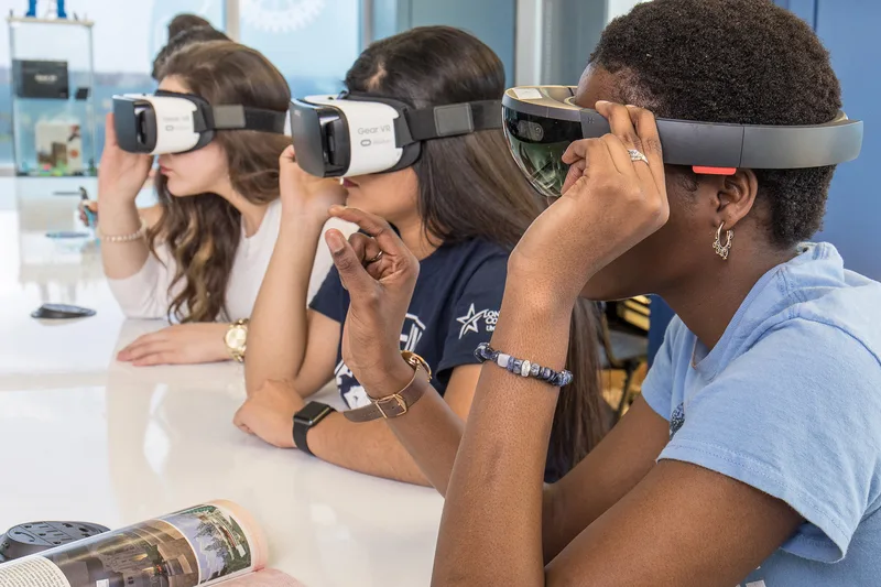Women wearing Samsung Gear VR and HoloLens vision goggles at white table