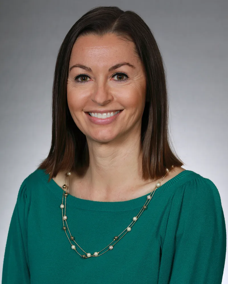 Professional headshot smiling brunette woman teal knit top layered pearl necklace