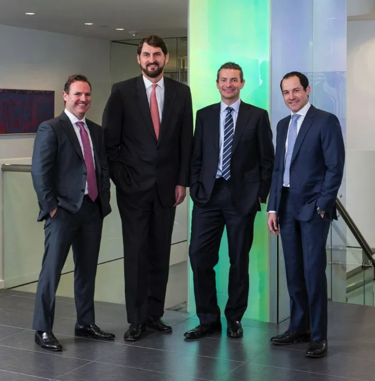 four suited executives posing for corporate group portrait in modern glass lobby
