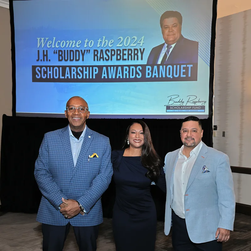 Three formally attired professionals posing before scholarship awards banquet projection screen