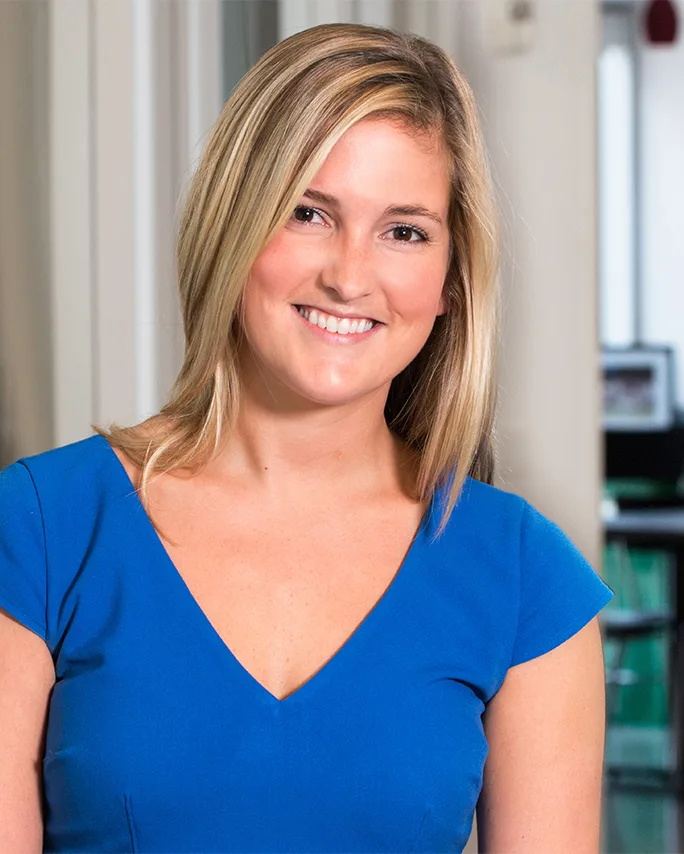 Corporate headshot smiling woman blue top soft blurred office background