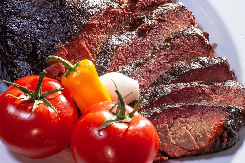 Sliced smoked brisket dark bark crust served with vine tomatoes and yellow pepper