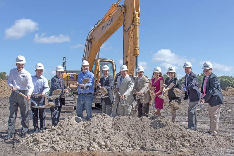 Corporate groundbreaking ceremony group with shovels and Hyundai excavator backdrop