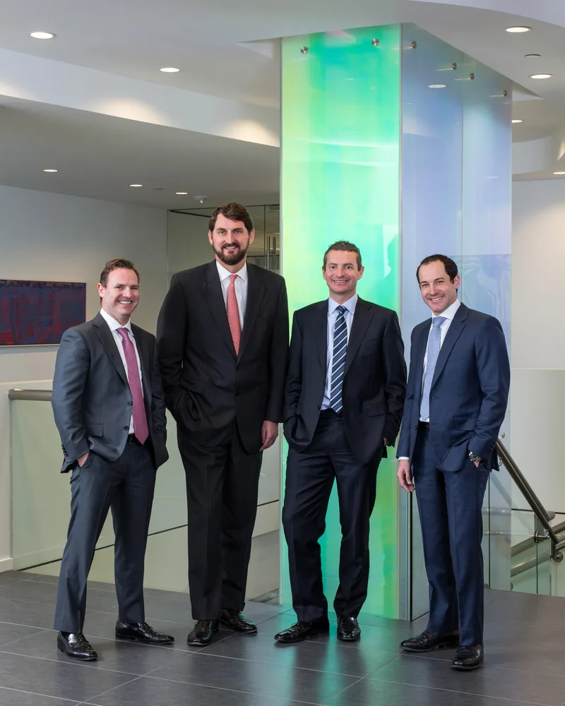 Corporate group portrait four executives in dark suits before glowing green glass column