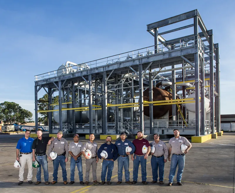 Enerflex team holding hard hats before steel-framed industrial process skid