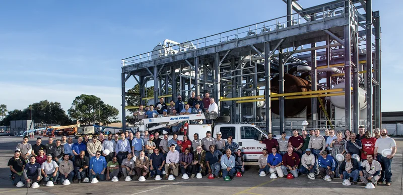 Enerflex workforce assembled at steel-framed industrial plant with large pressure vessels