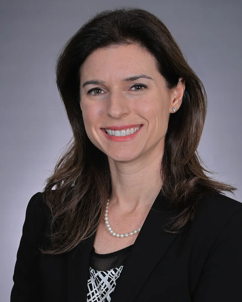 Corporate headshot of woman in black blazer and pearl necklace