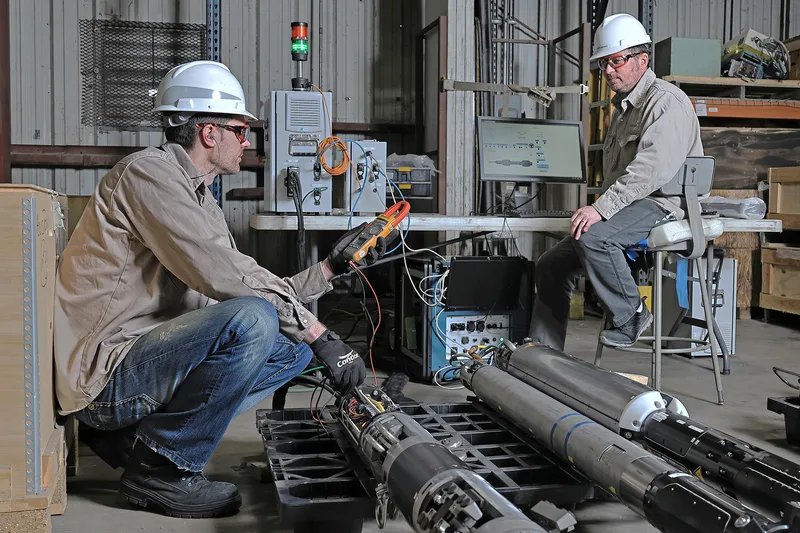 Equipment testing technicians using clamp meter on cylindrical black metal instruments
