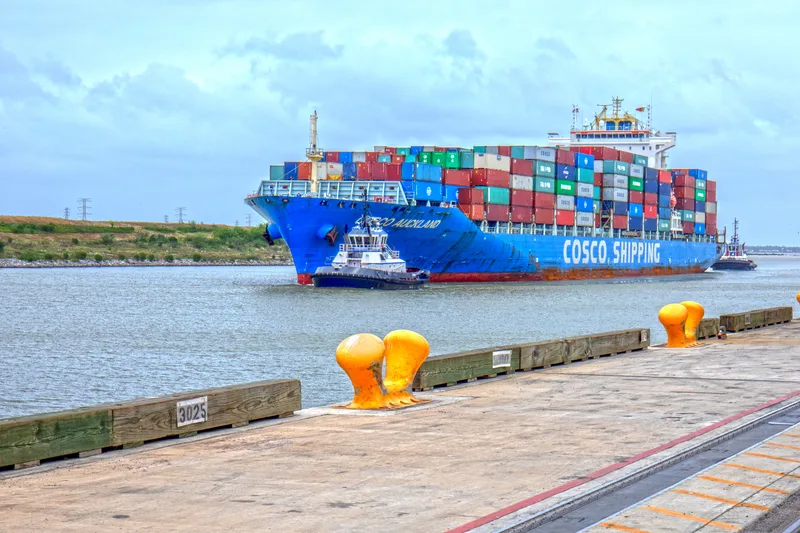 COSCO Auckland container ship loaded with multicolor cargo escorted by tugboats