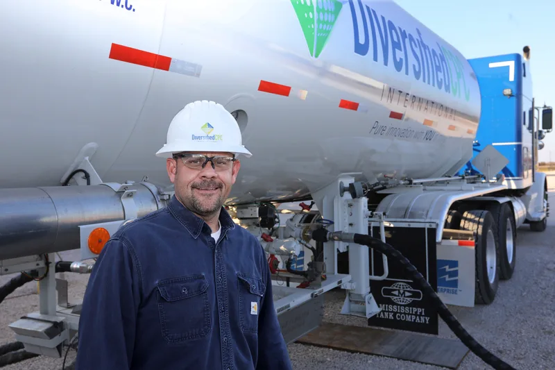 Gas purification worker in hard hat beside stainless steel tanker truck