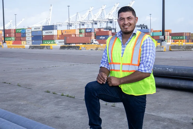 ILA worker in hi-vis safety vest smiling at busy shipping container terminal
