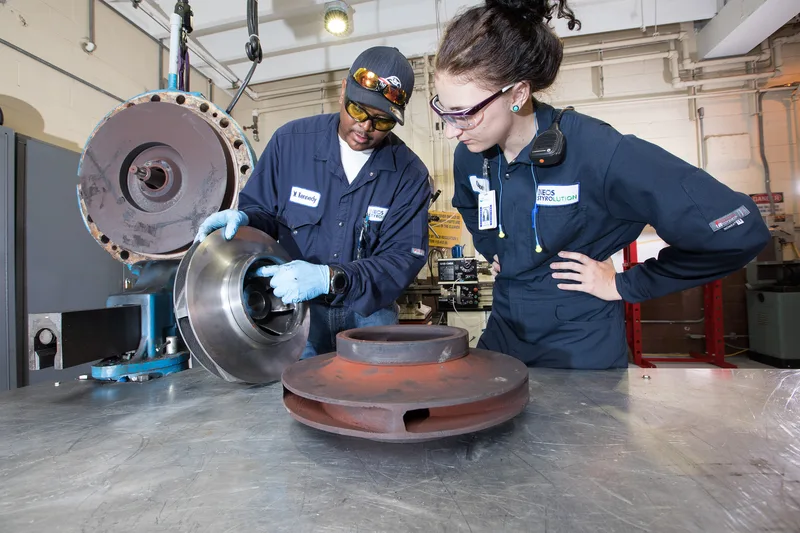 Equipment repair workers examining cast iron impeller beside machined steel disc