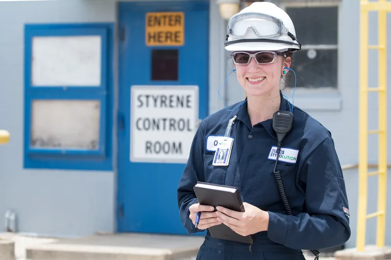 Industrial intern in hard hat safety goggles and navy coveralls smiling outdoors