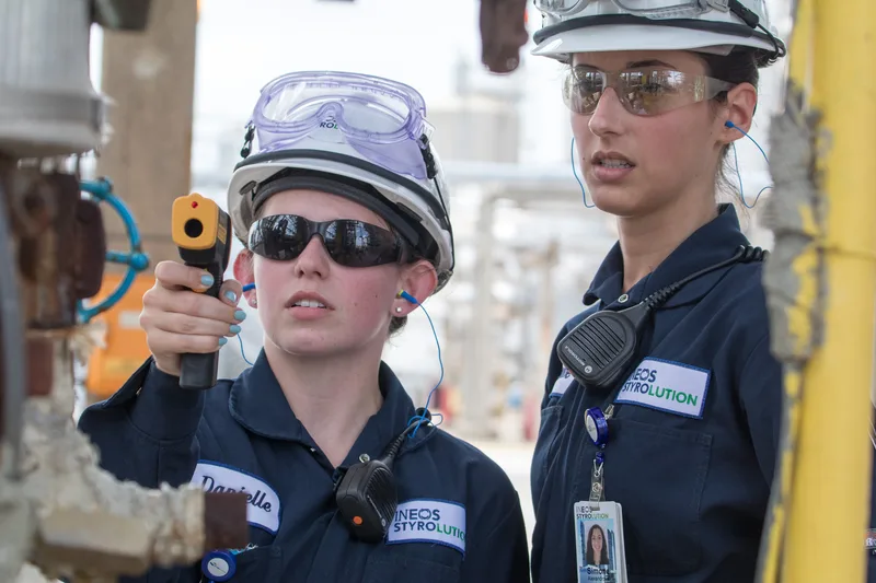 Interns in navy coveralls and hard hats scanning industrial pipes with infrared thermometer