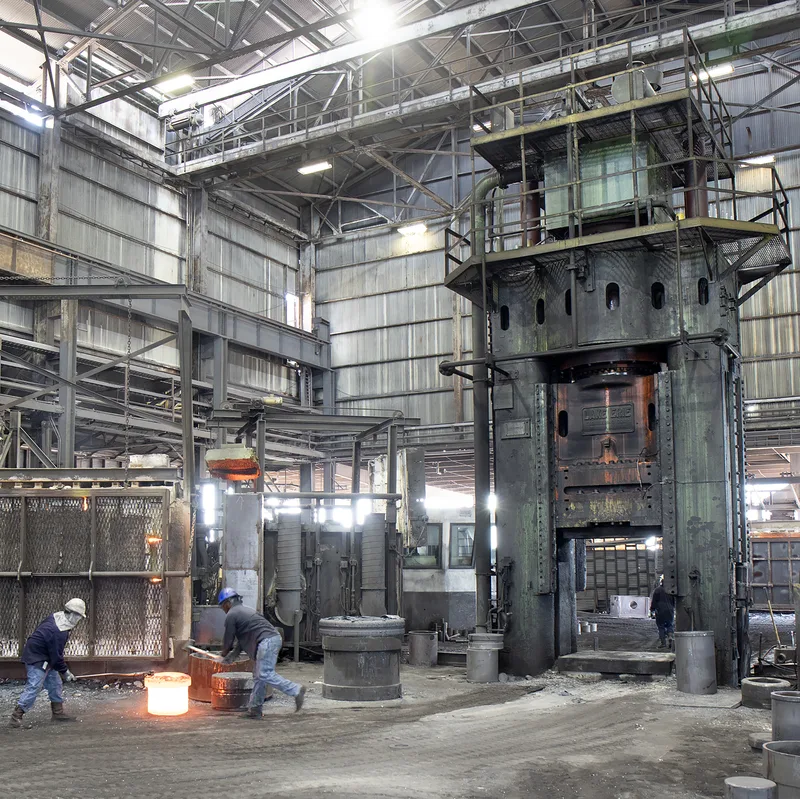 Large furnace hydraulic forging press workers handling glowing molten iron castings