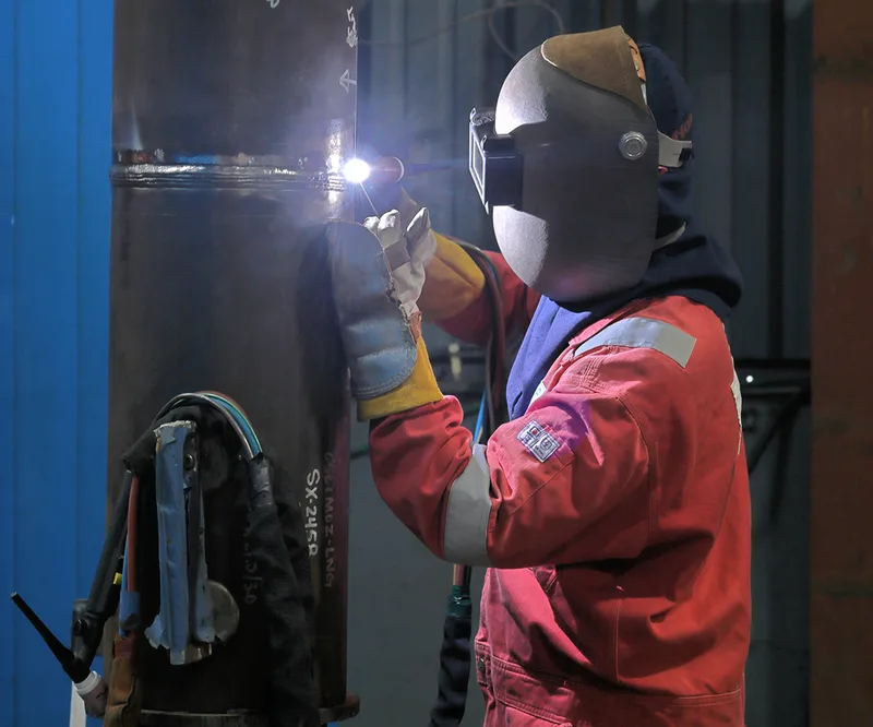 Manual welding technician joining large diameter steel pipe in industrial facility