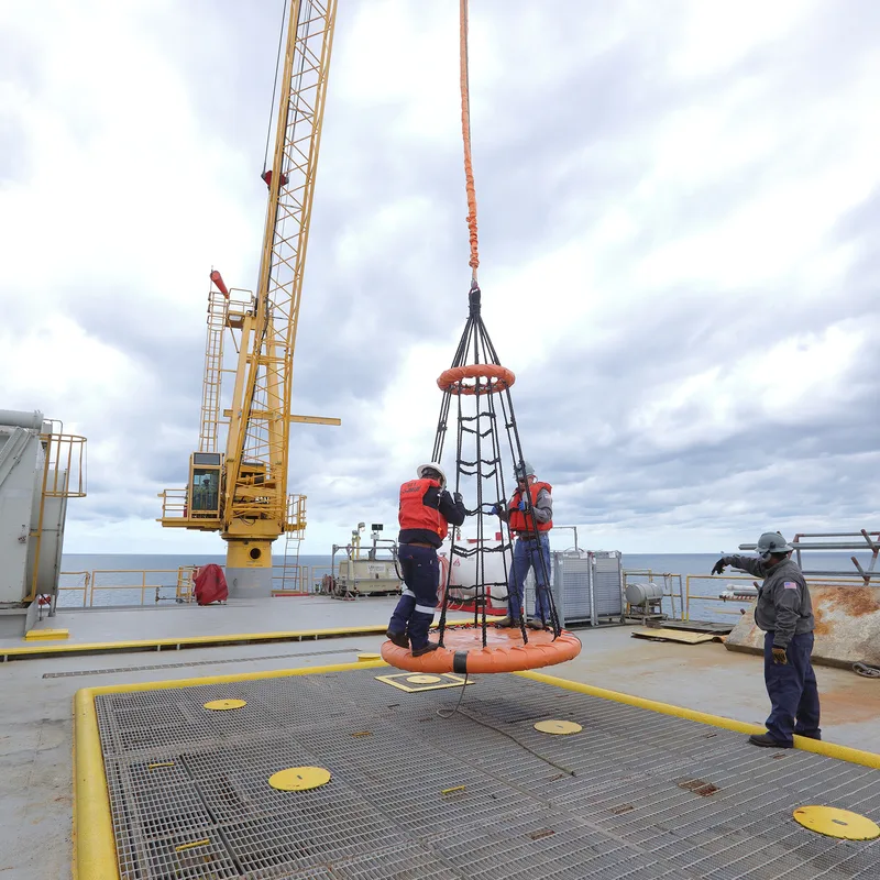environmental portrait of offshore platform workers guiding crane-lifted rescue basket