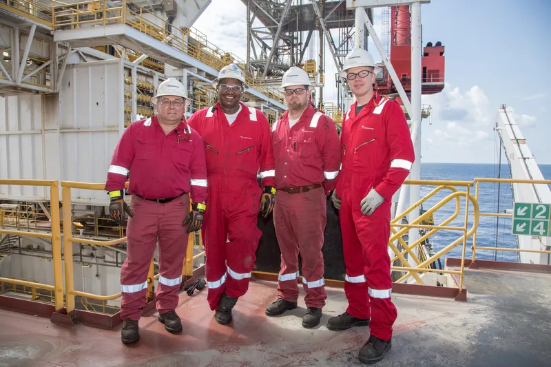 Environmental portrait four workers red coveralls hard hats offshore platform deck