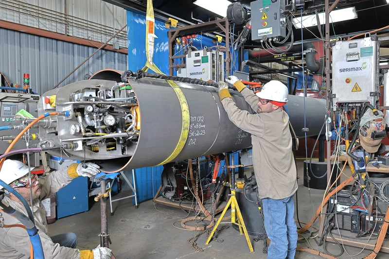 Automatic pipe welding technicians fitting orbital clamp on large coated steel pipe