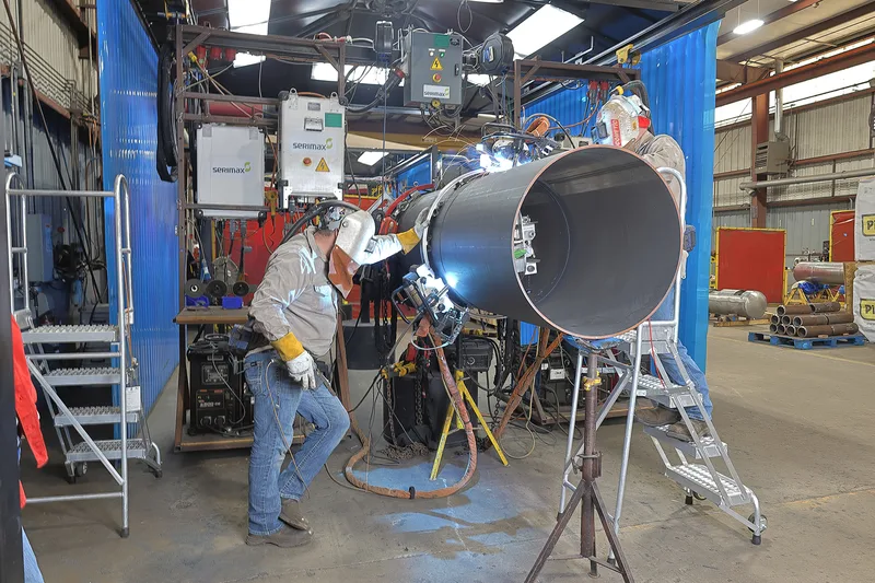 Automatic pipe welding technicians joining oversized black steel section with orbital welder