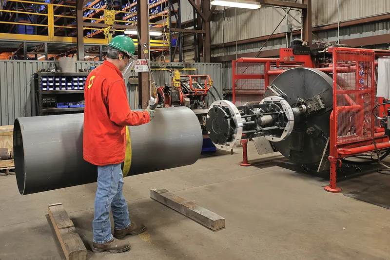 industrial worker feeding black steel pipe into Serimax beveling machine