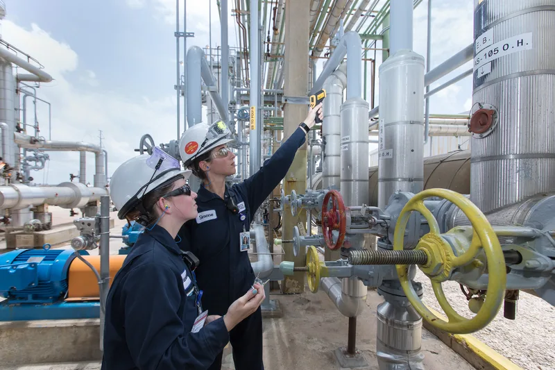 Interns inspecting industrial pipe valves with infrared thermometer at refinery