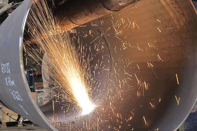 plasma cutting inside large steel pipe with bright cascading sparks