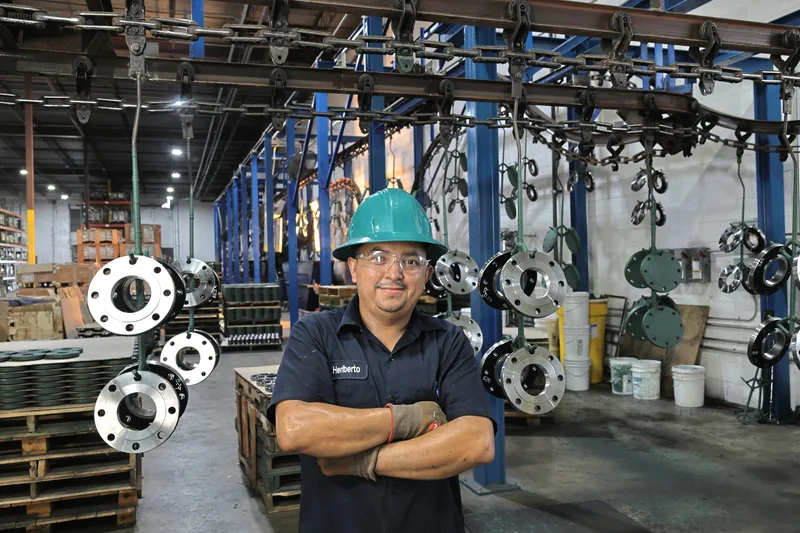 Confident worker in hard hat among stainless steel flanges on overhead conveyor
