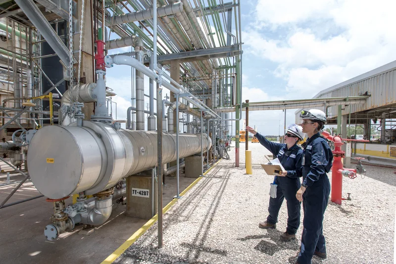 interns inspection stainless steel heat exchangers amid overhead industrial piping network