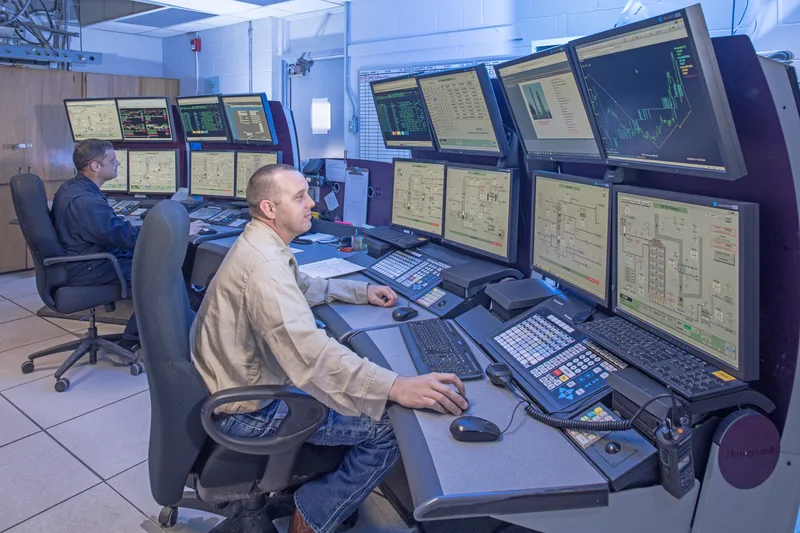 Operators at styrene process control console with multiple industrial monitoring screens
