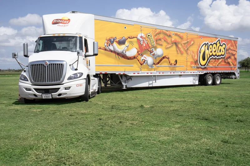 FritoLay tractor pulling vibrant Cheetos-branded trailer wrap on open field