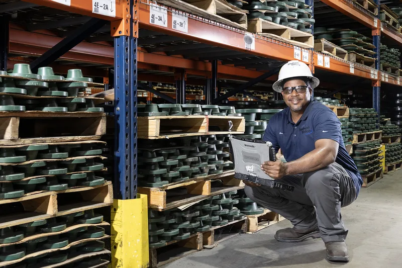 warehouse worker holding rugged tablet among stacked green cast iron valve flanges