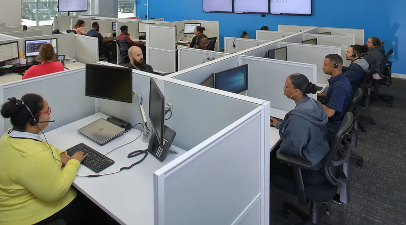 Call center agents at cubicle workstations with headsets and dual monitors