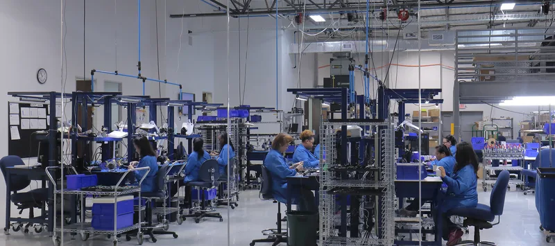 Electronic assembly floor with blue-coated technicians at overhead-wired production workstations