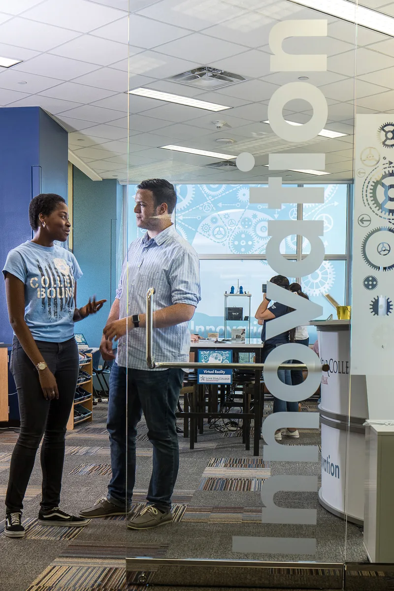 Two professionals in candid conversation inside glass-walled innovation workspace